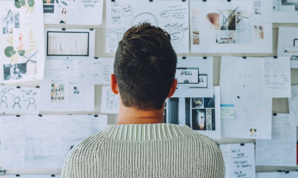 man staring at a wall full of papers and research; How to Do Research When Writing a Fictional Book