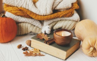 green book with candle on top and cozy blankets folded behind with fall leaves on the table; how to create a BookTok account