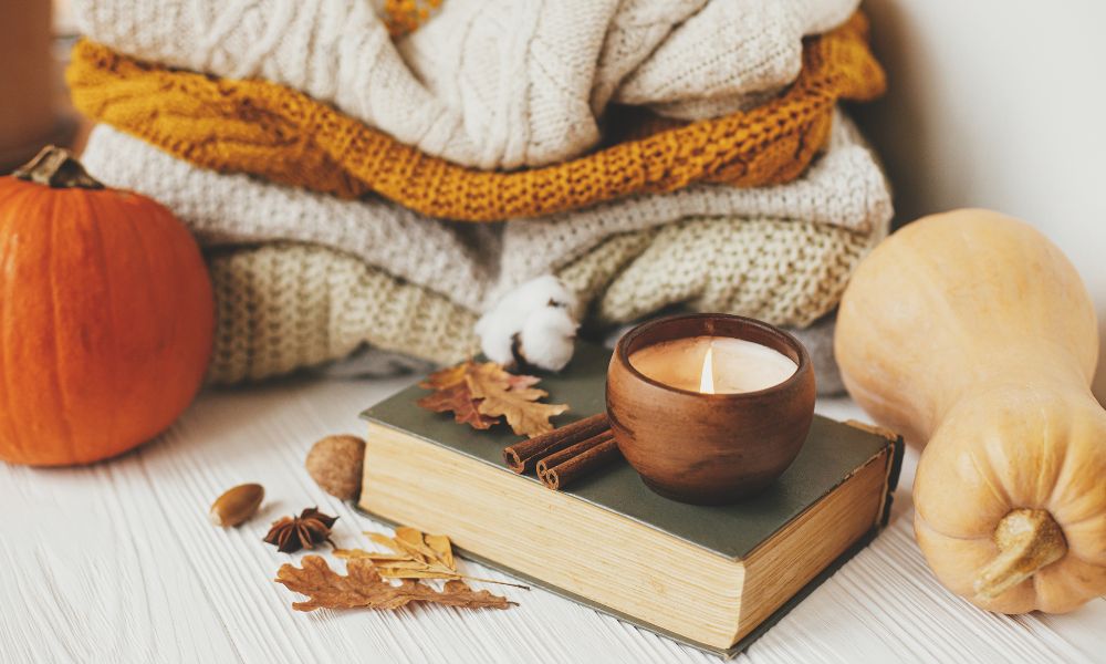 green book with candle on top and cozy blankets folded behind with fall leaves on the table; how to create a BookTok account