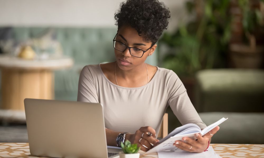 woman wearing glasses reviewing material on a laptop; manuscript review